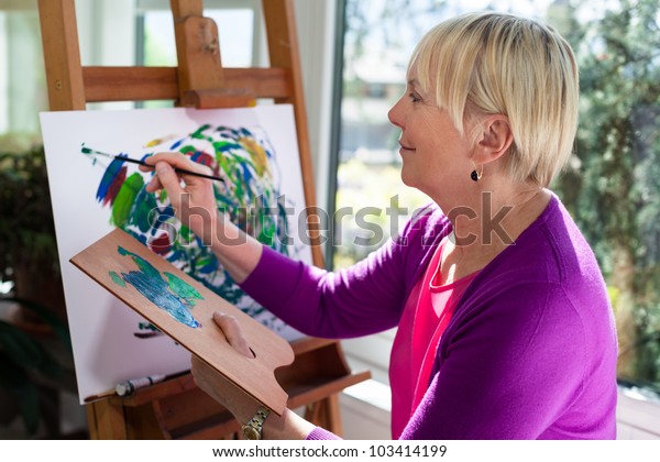 Happy\
retired woman painting on canvas for fun at\
home