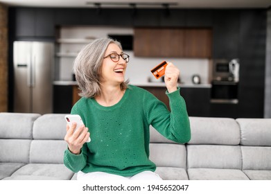 Happy retired woman spends savings on online shopping. Cheerful senior female holds smartphone and credit card in hands and making purchase online, using mobile app for buying - Powered by Shutterstock