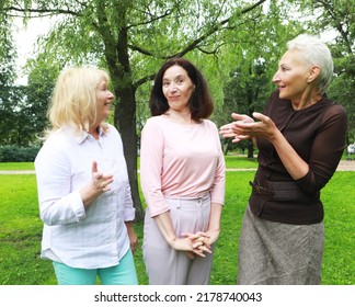 Happy Retired Women Meet In The Park. Two Women Friends In The Park Congratulate The Third Woman.