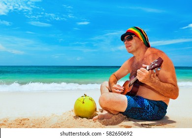 Happy Retiree Age Man In Funny Hat Has Fun, Play Reggae Music On Hawaiian Guitar, Enjoy Caribbean Beach Party. Seniors Lifestyle And Leisure. Travel Family Activity On Jamaica Island Summer Holiday.
