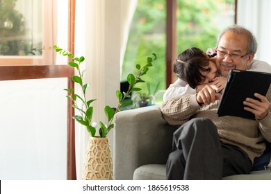 Happy retirement elderly man sitting on sofa at living room with granddaughter using digital tablet together. Multigenerational family with technology concept. - Powered by Shutterstock