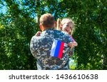 Happy reunion of soldier from Russia with family, daughter hug father. A little girl holds the flag of Russia in her hand