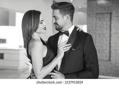 Happy rich 30s woman holding sexy boyfriend in tuxedo black and white