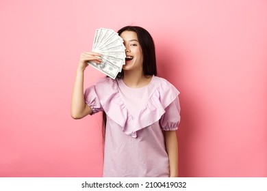 Happy Rich Asian Woman Showing Money And Smiling, Shopping With Cash, Standing In Dress Against Pink Background