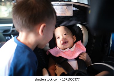 Happy Road Trip With Young Kid, Big Brother And Little Sister Playing Together In Car, Cute Smiling Asian Baby Girl Child Sitting In Rear Facing Car Seat.