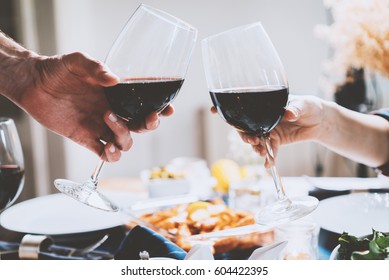 Happy Romantic Couple Cheering With Glasses Of Red Wine At Restaurant, People Making Cheers And Celebrating Anniversary Or Engagement, Traditional Or Togetherness Concept