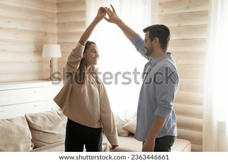 Happy romantic couple dancing at home, enjoying leisure time, moving to music, smiling man holding beautiful woman hand, leading in dance, family having fun, celebrating anniversary or relocation