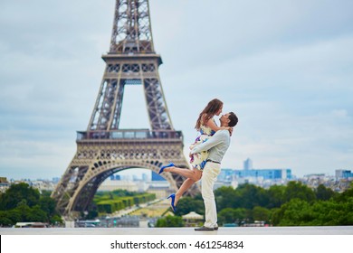 Happy romantic couple hugging near the Eiffel tower in Paris, girl is jumping, Tourists enjoying their vacation to France