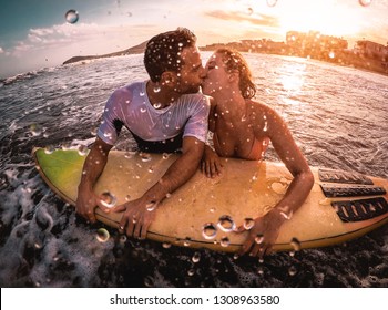 Happy romantic couple kissing while surfing in the ocean - Sporty surfers bodyboarding and having a tender moment in the water  - Extreme sport, love, relationship and healthy lifestyle concept  - Powered by Shutterstock