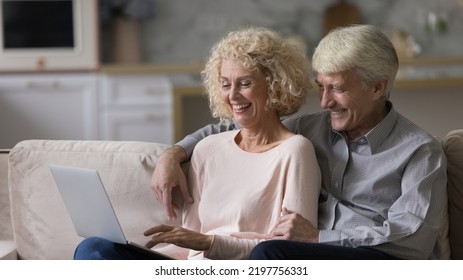 Happy Romantic Mature Couple Relaxing On Home Couch Together, Using Laptop Computer, Laughing, Watching Movie, Talking On Video Call, Shopping With Online App. Internet Communication. Banner