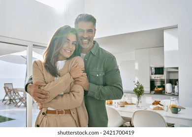 Happy romantic mature older Latin man and woman in their 50s, smiling affectionate loving middle aged couple hugging looking at camera standing together in modern kitchen at home. Portrait. - Powered by Shutterstock