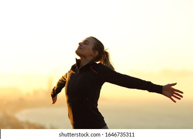 Happy runner breathing fresh air outstretching arms at sunset in the city outskirts