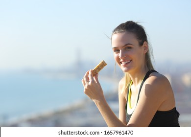 Happy Runner Eating Protein Bar Looking At Camera In A Sunny Day