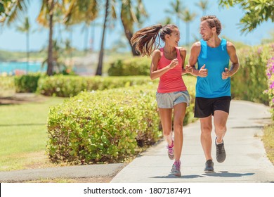 Happy runners couple running together talking training outside on city sidewalk. Woman and man jogging healthy cardio workout lifestyle. - Powered by Shutterstock