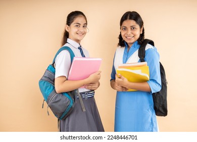 Happy Rural and Modern Indian student schoolgirls wearing school uniform holding books and bag standing together isolated over beige background, Studio shot, Education concept. - Shutterstock ID 2248446701