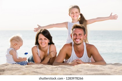 Happy Russian Family Of Four Lying Together On Beach Vacation 
