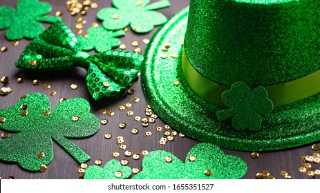 Happy Saint Patrick's Day greeting card with traditional symbols, shamrock, green attire. Green hat, bow tie, St Patricks Day shamrocks, golden confetti on dark wooden background, copy space - Powered by Shutterstock