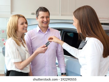 Happy Saleswoman Handing Over Car Keys To The Attractive Young Family