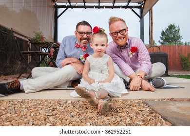 Happy Same Sex Couple Sitting With Daughter Outdoors