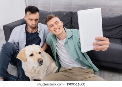 Happy Same Sex Couple Taking Selfie On Digital Tablet Near Labrador In Living Room