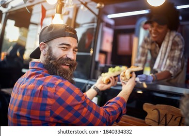 Happy, Satisfied Caucasian Beardy Male Customer Taking  Sandwiches From A Polite Employee In Fast Food Service, Looking At Camera, Laughing. Eye Contact