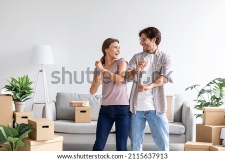Happy satisfied caucasian man and wife celebrating buying of new apartment, dancing in room interior with cardboard boxes. Couple have fun after moving at own apartment. Rent flat, mortgage and loan