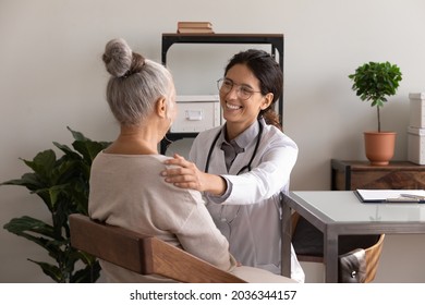 Happy satisfied GP doctor telling good news to elder patient, congratulating on optimistic medical checkup result, giving support, empathy, touching shoulder of senior woman at appointment in office