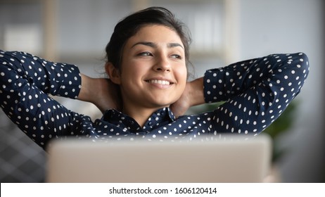Happy satisfied indian woman rest at home office sit with laptop hold hands behind head, dreamy young lady relax finished work feel peace of mind look away dream think of future success concept
