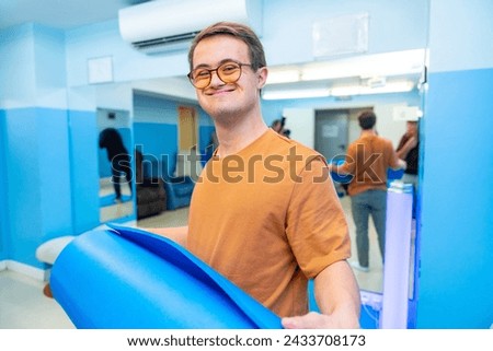 Happy and satisfied man with down syndrome after yoga class holing a mat