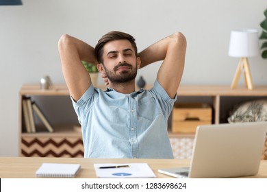 Happy satisfied man taking break to lounge relax finished work at home, calm young guy holding hands behind head sitting at desk resting breathing fresh air enjoying no stress free relief day concept