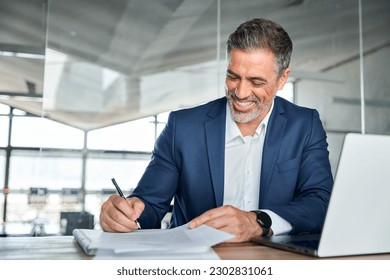 Happy satisfied middle aged professional business man executive ceo manager, lawyer wearing suit sitting at desk signing law document writing signature making legal agreement corporate deal in office. - Powered by Shutterstock