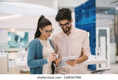 Happy Satisfied Young Couple Looking At New Arrivals In Tech Store.