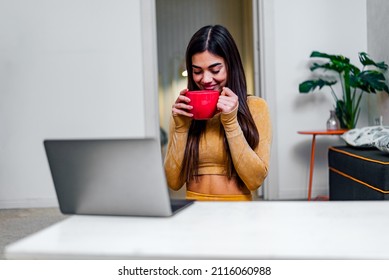 Happy Satisfied Young Woman Enjoying Cup Of Coffee At Home While Using Laptop Smiling Girl Drinking Tea Or Hot Chocolate While Making Online Video Call Or Surfing The Web Internet