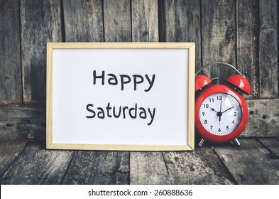 Happy Saturday Message On White Board And Red Retro Clock  By Wooden Background.