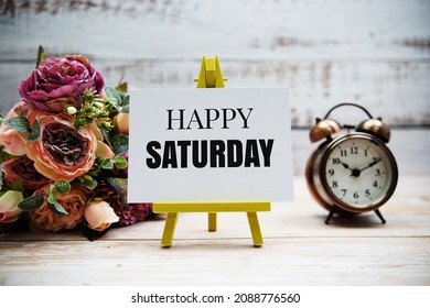 Happy Saturday Text With Flower Bouquet And Alarm Clock On Wooden Background