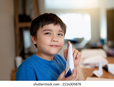 Happy school boy looking at camera with smiling face while showing origami Swan paper. Kid learning paper art origami lesson, Child having fun doing Art and Craft at home, Home schooling concept