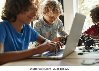 Happy School Boy Student Making Robotic Car Sitting At Table At STEM Class. Diverse Children Learning Programming Using Computers And Constructing Robots At Science And Coding Education Tech Lesson.