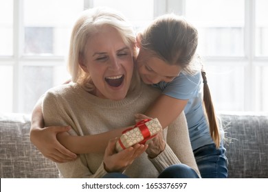 Happy school girl granddaughter cuddling hugging embracing from back excited surprised middle aged retired grandmother with gift box in hands head shot. Mothers day, birthday celebration concept. - Powered by Shutterstock