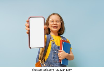 Happy School Kid Is Showing Smartphone On Background Of Blue Wall. Blank Screen Mobile Phone For Graphic Montage.