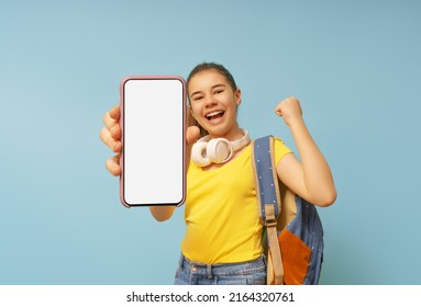 Happy School Kid Is Showing Smartphone On Background Of Blue Wall. Blank Screen Mobile Phone For Graphic Montage.