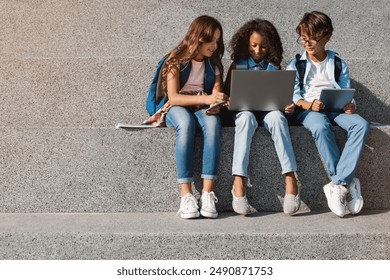 Happy school kids preteen boys and girls elementary middle pupils children sitting on the stairs and looking in laptop screen with digital devices gadgets tablet smartphone in hands outdoors. - Powered by Shutterstock