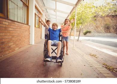 Happy school kids pushing a boy on wheelchair in school corridor - Powered by Shutterstock