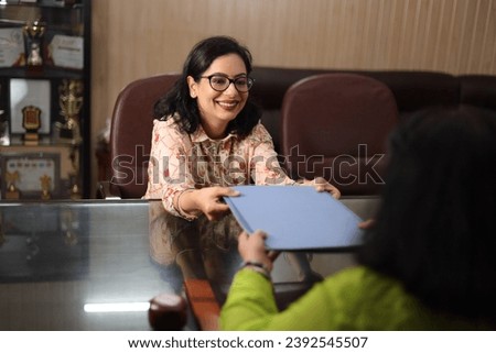Happy school Principal mam passing the file, report card of a student to the parent, PTM, Parents teacher meeting, smiling.