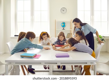 Happy school teacher and first grade students having interesting engaging activities in class. Little children sitting around big classroom table, learning ABCs, talking and playing fun games together - Shutterstock ID 2018895593