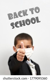 Happy Schoolboy In Face Mask. Mixed-race Kid Shows Thumbs-up Gesture Between Pile Of Books. Back To School After Covid-19. School Year Start After Long Delay Due To Coronavirus