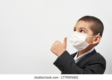 Happy Schoolboy In Face Mask. Mixed-race Kid Shows Thumbs-up Gesture Between Pile Of Books. Back To School After Covid-19. School Year Start After Long Delay Due To Coronavirus