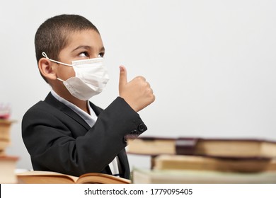 Happy Schoolboy In Face Mask. Mixed-race Kid Shows Thumbs-up Gesture Between Pile Of Books. Back To School After Covid-19. School Year Start After Long Delay Due To Coronavirus