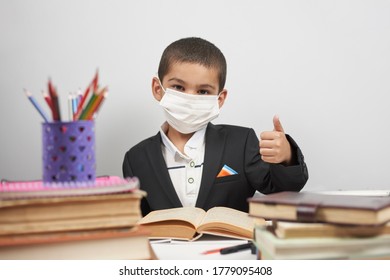 Happy Schoolboy In Face Mask. Mixed-race Kid Shows Thumbs-up Gesture Between Pile Of Books. Back To School After Covid-19. School Year Start After Long Delay Due To Coronavirus