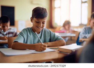 Happy schoolboy writing while learning during a class in the classroom. - Powered by Shutterstock