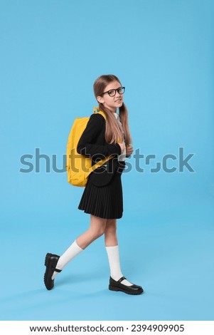 Happy schoolgirl with backpack on light blue background